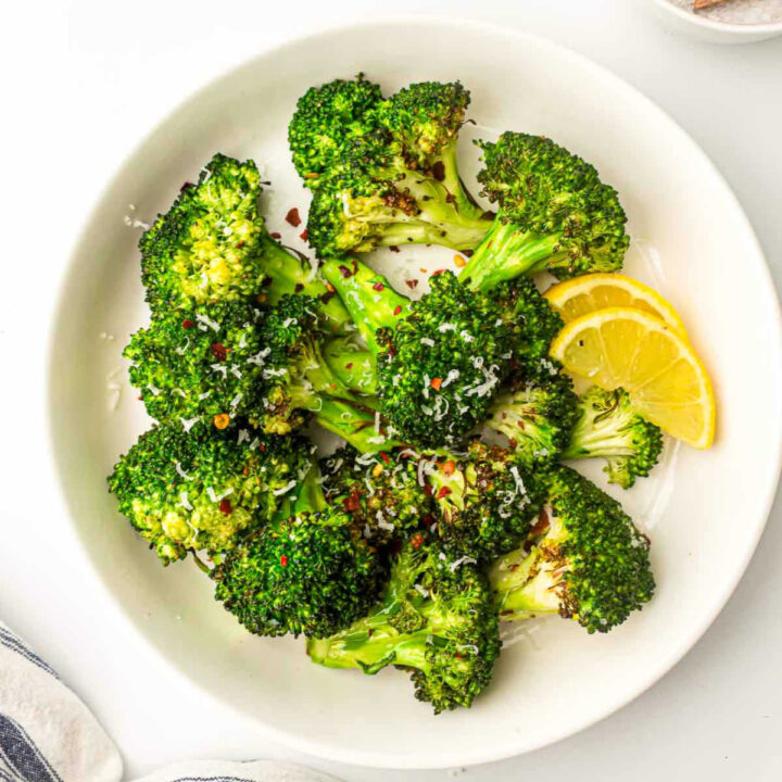 Air fried broccoli on a white plate with lemon wedges.
