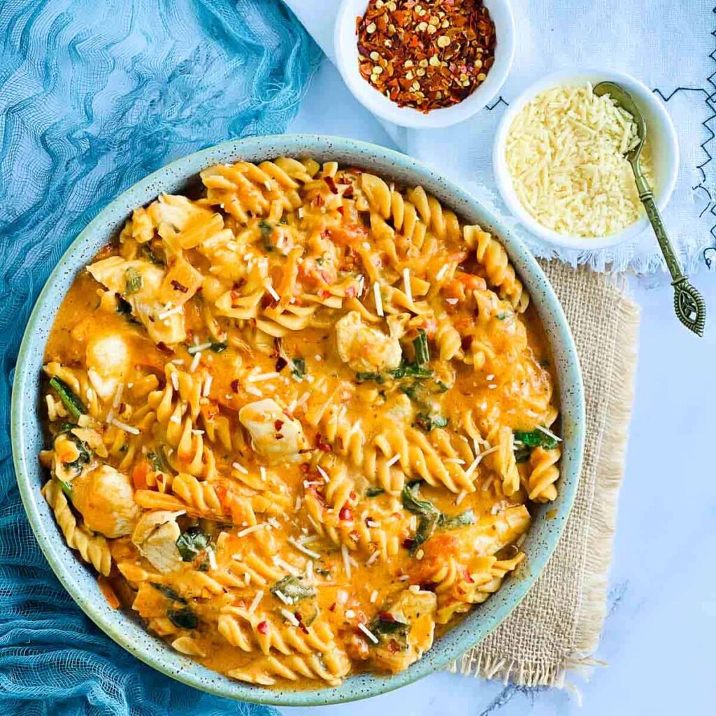 An overhead shot of a large bowl of creamy chicken and fusilli pasta in a tomato cream sauce, sprinkled with Parmesan cheese and red pepper flakes.