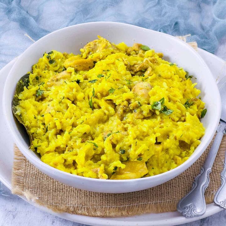 A white bowl filled with bright yellow chicken khichdi, a comforting dish of rice, lentils, and chicken cooked with turmeric and spices, garnished with fresh cilantro, sitting on a burlap mat.