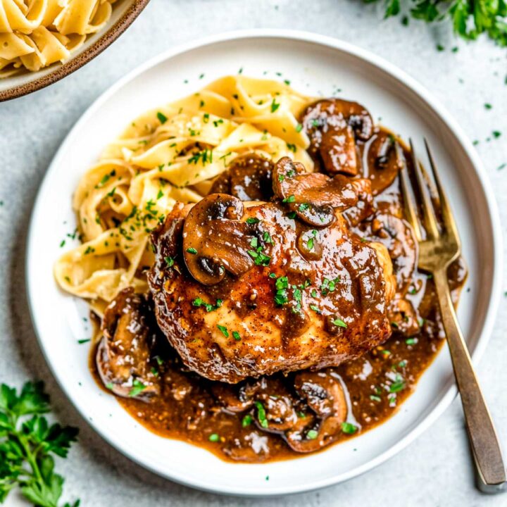 Chicken marsala served over a bed of noodles on a white plate.