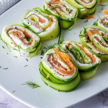 Close up of cucumber smoked salmon rolls on a white serving plate.