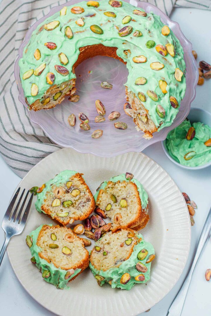 Sliced pistachio bundt cake on a serving plate with remaining cake in the background.