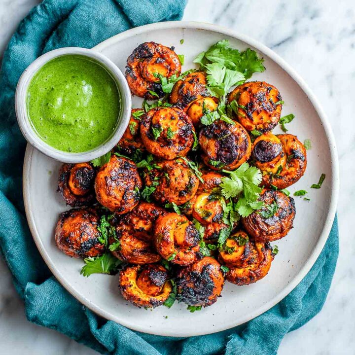 Tandoori mushrooms served on a white plate with mint chutney.