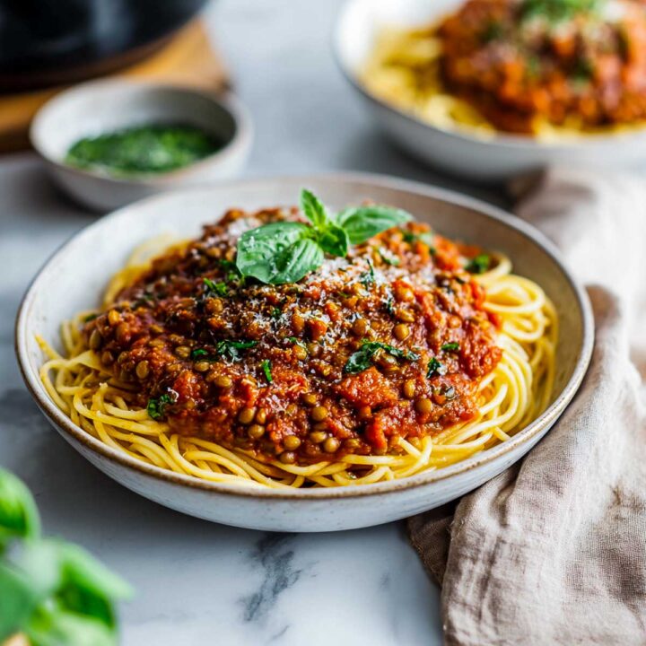 A bowl of spaghetti topped with a thick, chunky vegan Bolognese sauce made with lentils, tomatoes, and herbs, garnished with fresh basil leaves.