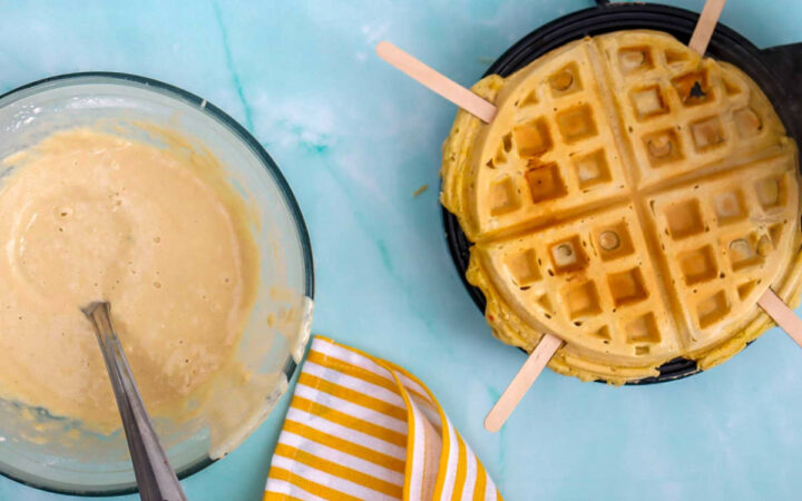Pouring waffle batter into the waffle maker with popsicle sticks in place for waffle pops.