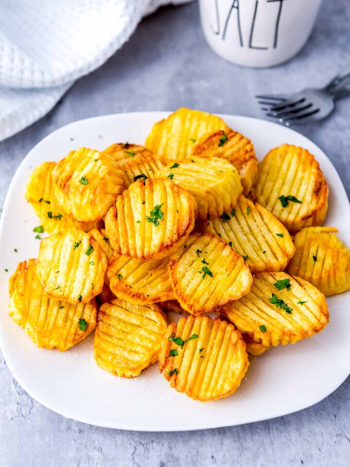 Golden, crispy, corrugated accordion-cut potatoes garnished with parsley on a white plate.