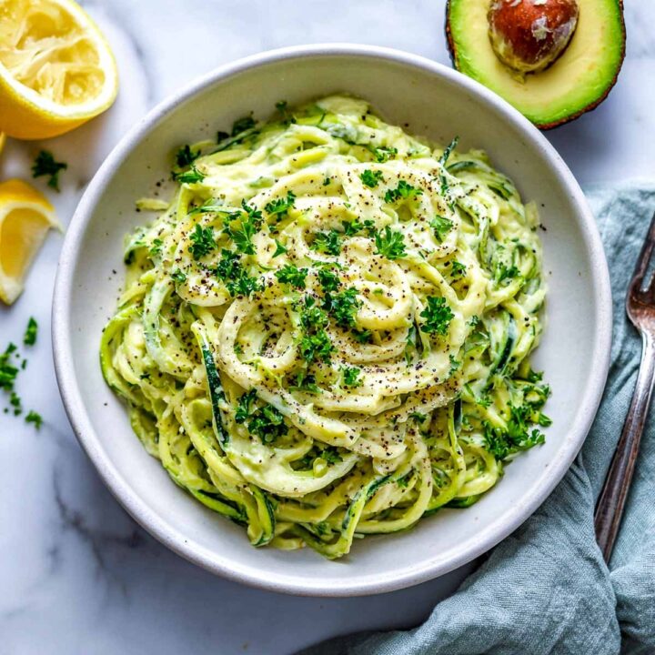 Zucchini noodles (zoodles) coated in a creamy green avocado alfredo sauce, seasoned with black pepper and garnished with fresh parsley.