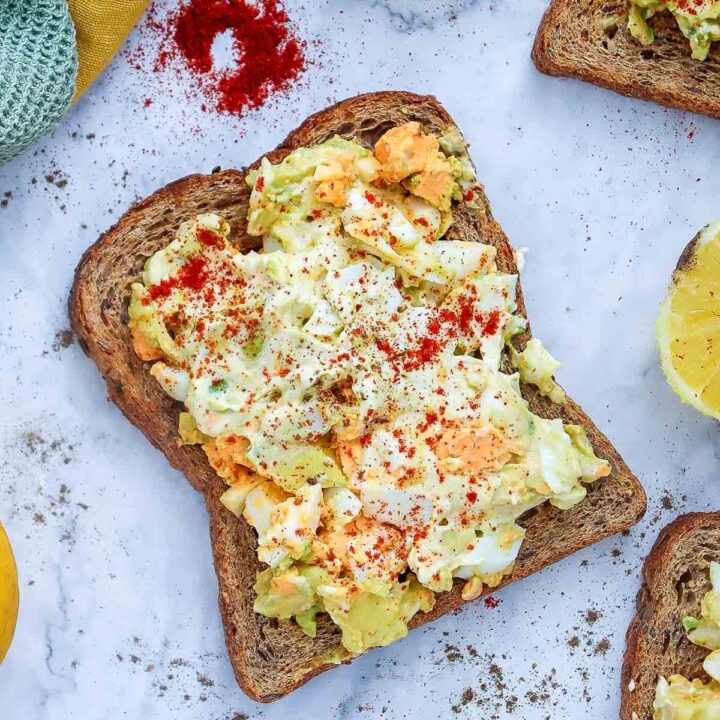 Open-faced sandwich with avocado egg salad on whole-wheat toast, sprinkled with paprika and black pepper.