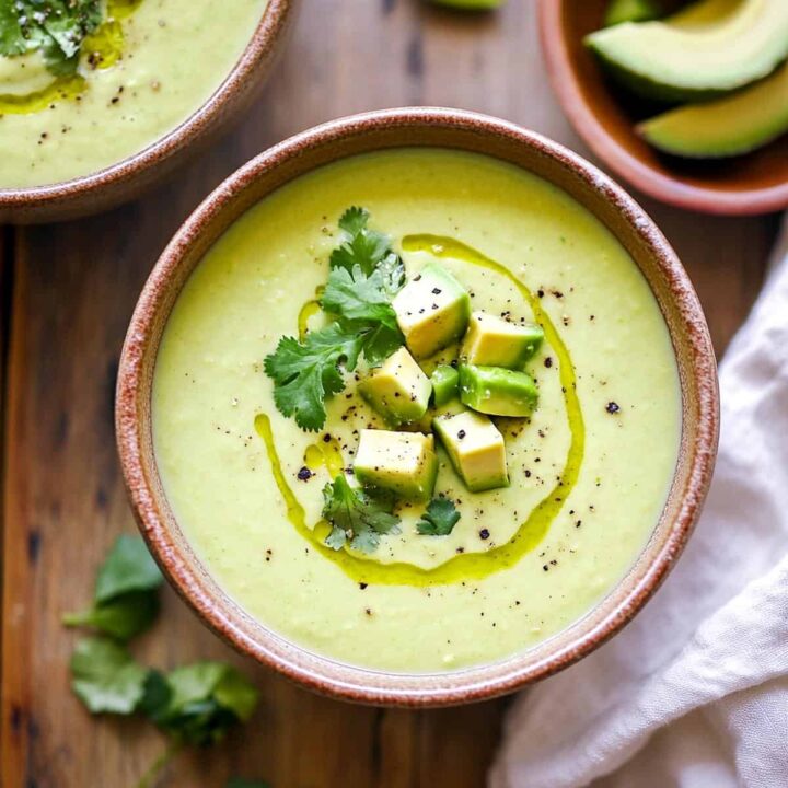 Close-up of a bowl of creamy green avocado lime soup, garnished with diced avocado, cilantro, and a drizzle of olive oil.
