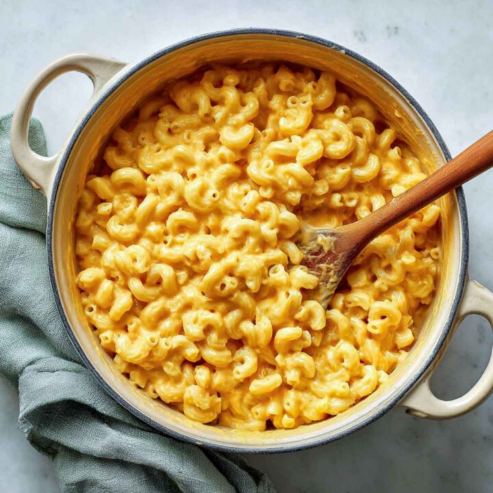 Creamy butternut squash mac and cheese mixture in cream pot being stirred with wooden spoon.