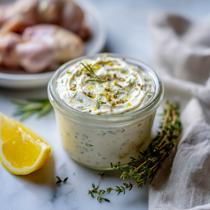 A jar of classic greek yogurt herb marinade with lemon and thyme in the background.