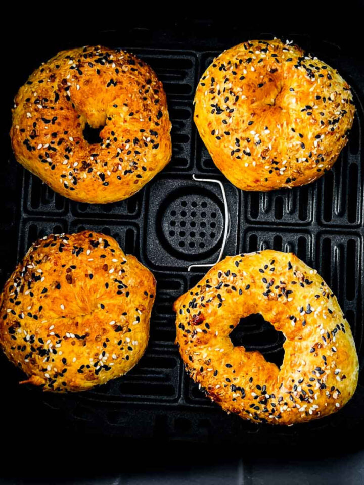 Four golden-brown, homemade cottage cheese bagels topped with sesame and black seeds, baked in the black basket of an air fryer.