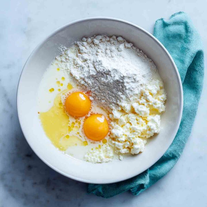 Cottage cheese, eggs, flour, milk, and melted butter in bowl before mixing.