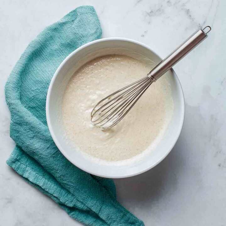 Smooth cottage cheese pancake batter in white mixing bowl with metal whisk.