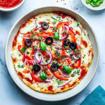 Cottage cheese pizza bowl with fresh toppings and bowls of sauce and peppers.