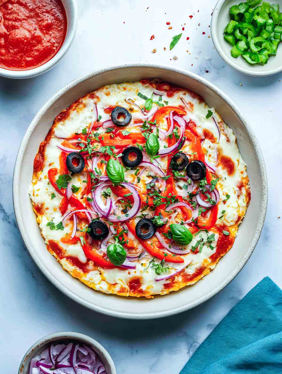 Crustless cottage cheese pizza bowl topped with peppers, onions, olives, and basil.