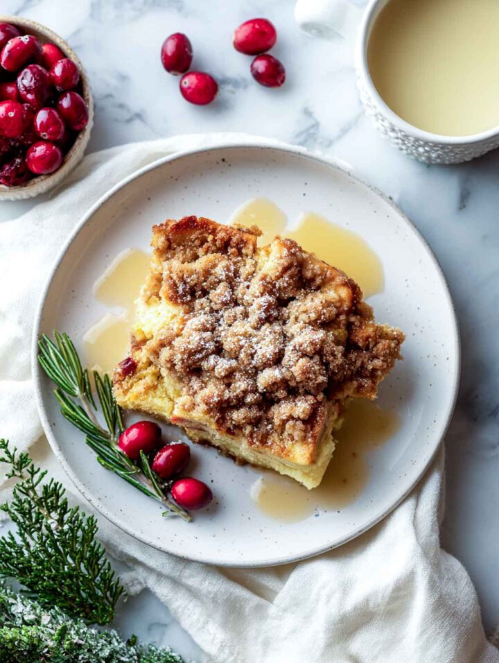 Slice of eggnog French toast casserole on plate with syrup and cranberries.