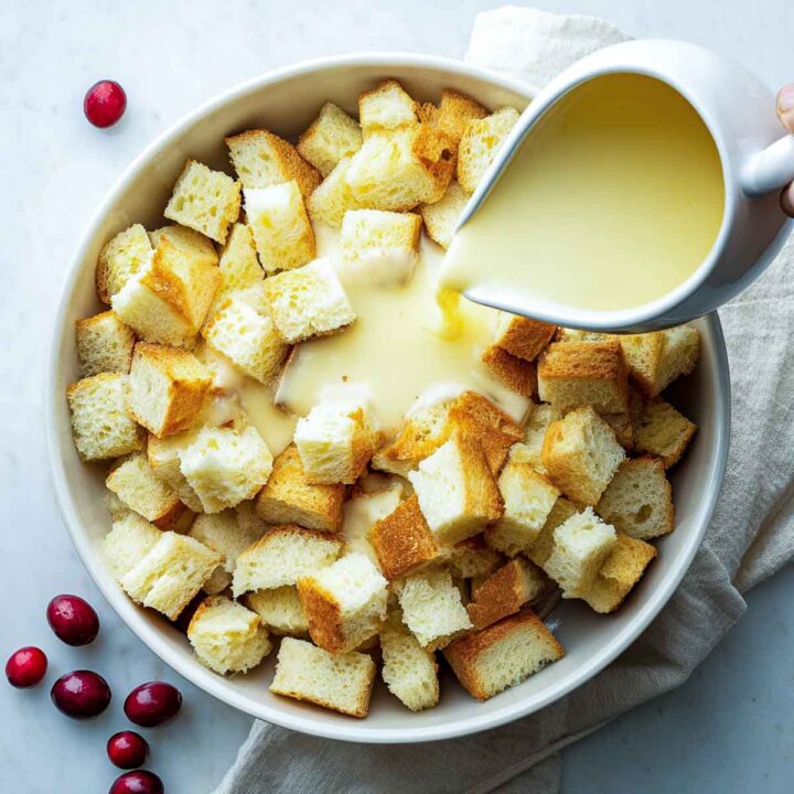 Eggnog custard being poured over brioche cubes for French toast casserole.