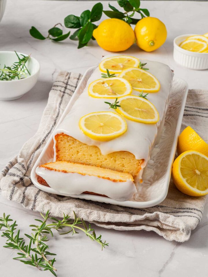 Lemon loaf cake on a white serving plate with a slice nearby.