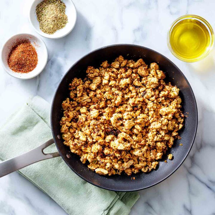 Cooked ground turkey seasoned with taco spices in a skillet on marble surface with small bowls of seasoning and olive oil beside.