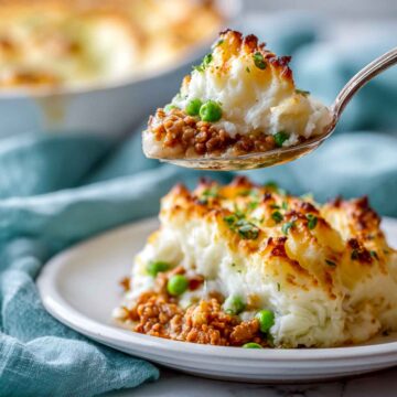Close-up of low-carb cottage pie on white plate showing creamy cauliflower mash and golden-brown turkey filling with peas.