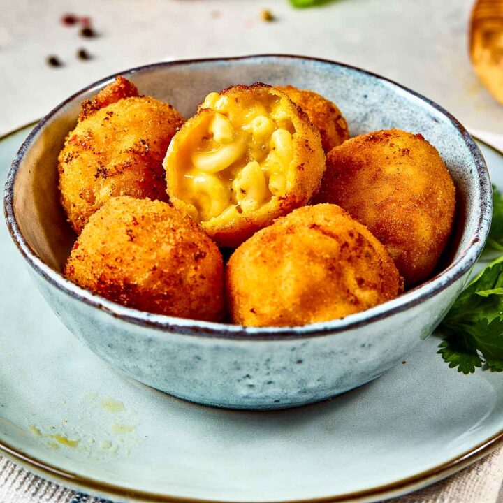 Close up of mac and cheese bites with one cut ball to show the inside.