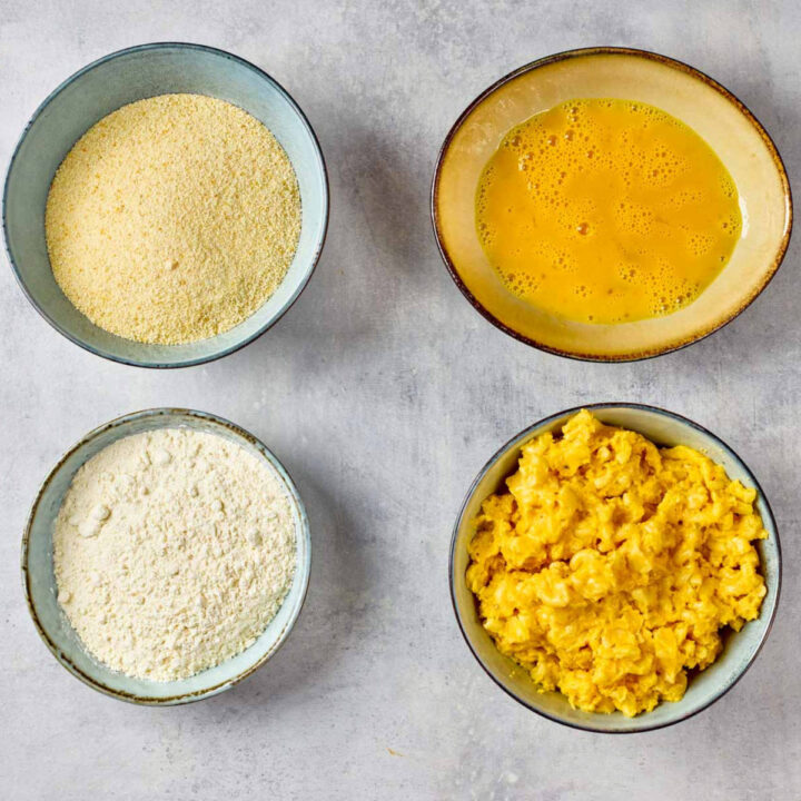 Cooled mac and cheese and breading station on a grey surface.
