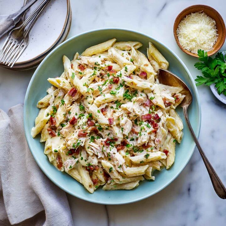 Creamy penne pasta with chicken and bacon bits, garnished with parsley in a blue bowl.