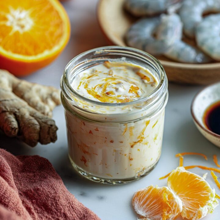 A jar of orange ginger yogurt marinade with shrimp in the background.