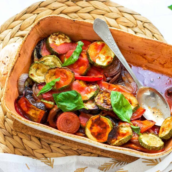 Baked ratatouille casserole with slices of zucchini, tomato, onion, and bell pepper, garnished with fresh basil.