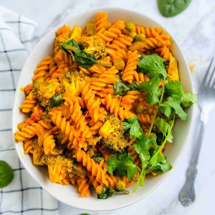 Red lentil fusilli pasta with curry sauce, broccoli, and spinach, garnished with cilantro.