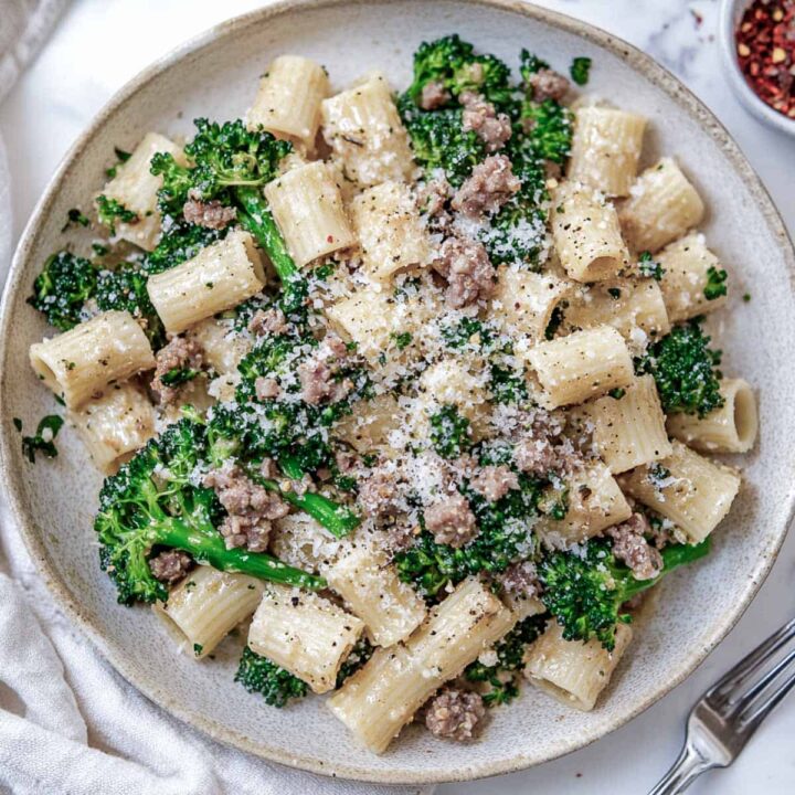 Rigatoni pasta with spicy sausage, broccolini, and grated cheese in a light gray bowl.