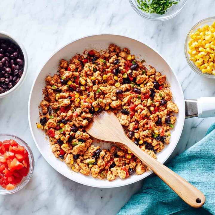 Ground chicken with beans, corn, and tomatoes cooking in skillet for Tex-Mex filling.