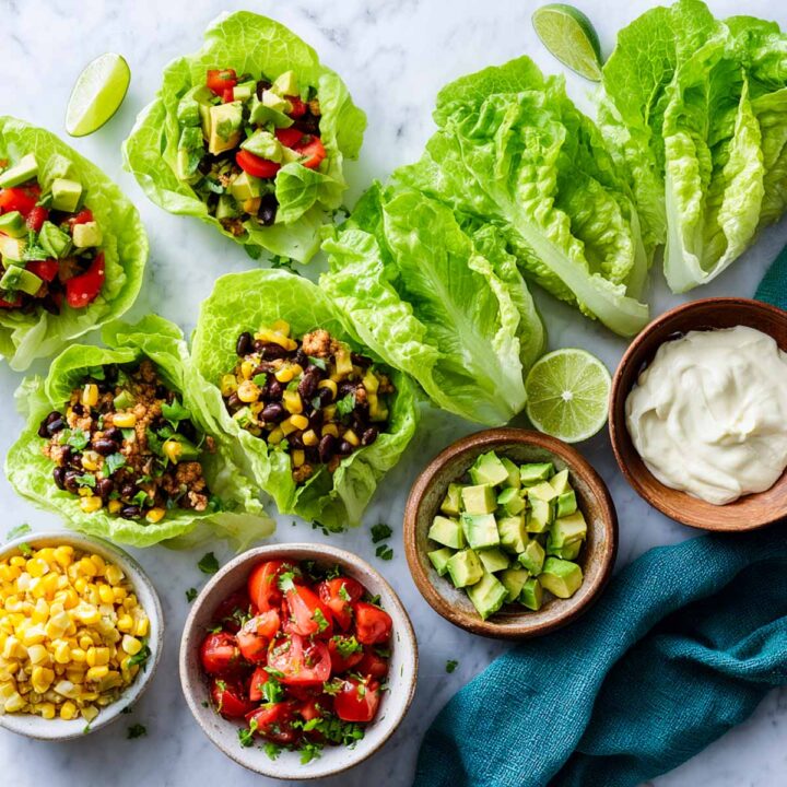 Partially filled lettuce leaves with Tex-Mex toppings and bowls of ingredients beside them.