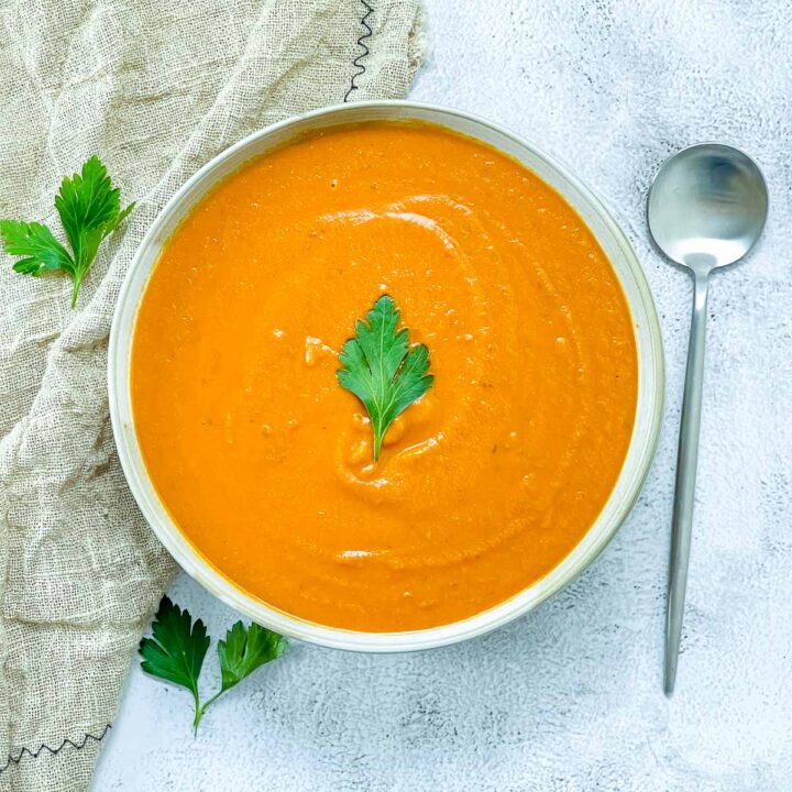 A bowl of creamy tomato lentil soup on a white marble surface.