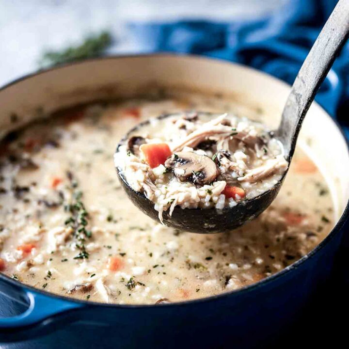 Ladle lifting hearty scoop of creamy turkey rice soup from Dutch oven.