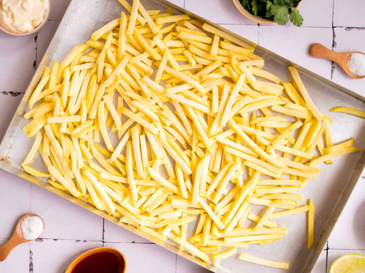 Cur fries spread on a baking sheet for seasoning.