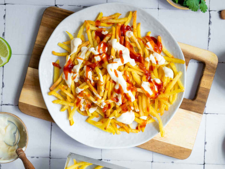 French fries on a serving plate topped with sauce.