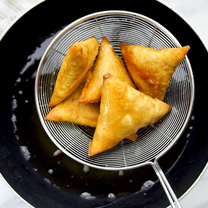 Golden-brown samosas being drained in a metal strainer after frying.