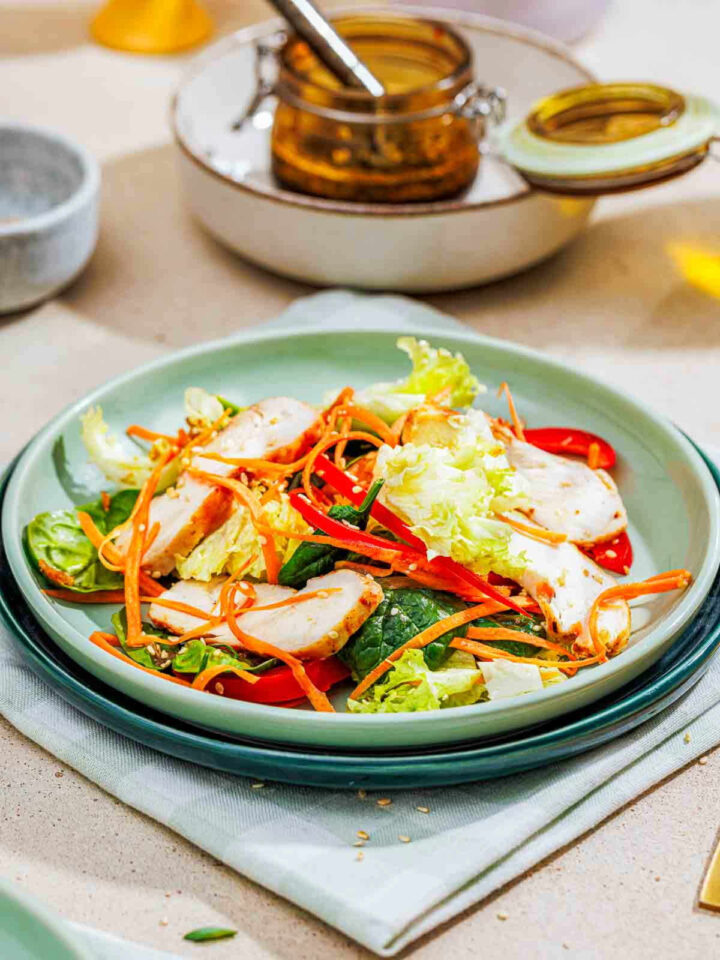 Sesame chicken salad with sliced breast, shredded carrots, and red peppers on a light green plate.