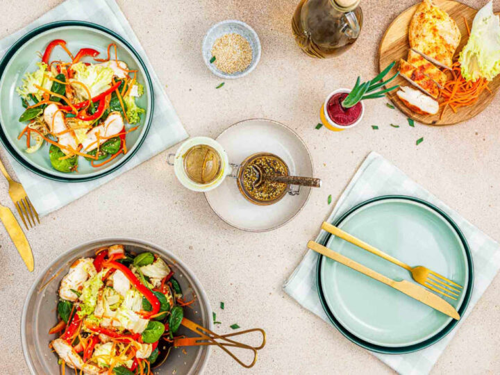 Table setting with a bowl of salad, plated servings, dressing jars, and gold utensils.