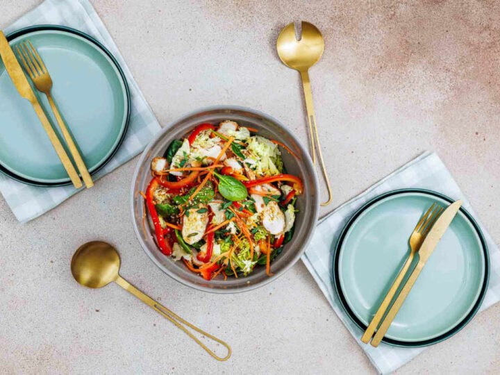 Overhead view of a large salad bowl centered between two place settings with gold serving spoons.