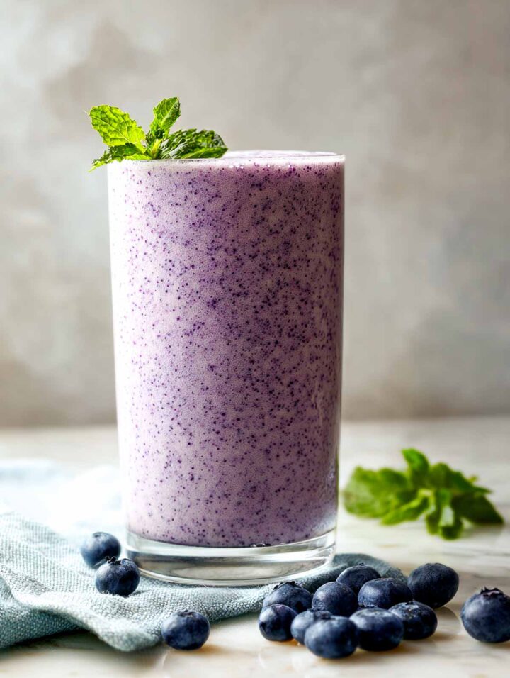 Side view of blueberry kefir smoothie in tall glass with mint and fresh berries.