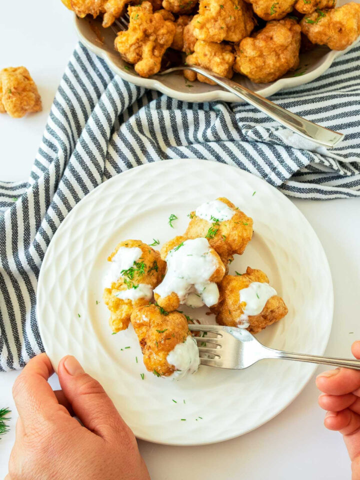 Person holding a fork and a plate with cauliflower bites on it.
