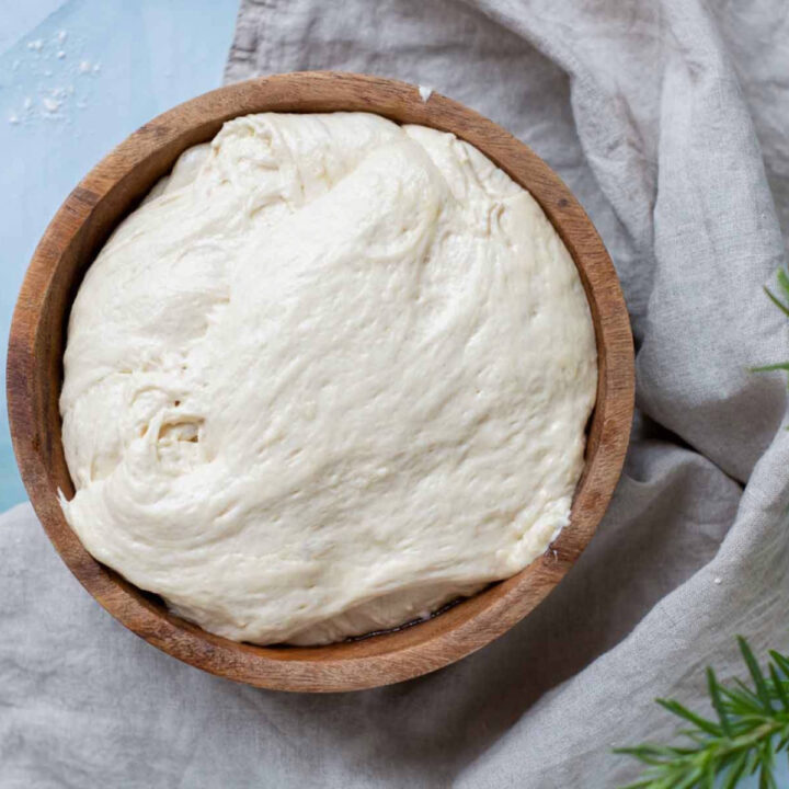 A top-down view of the focaccia dough after its rise, now significantly puffed up and filling the wooden bowl.