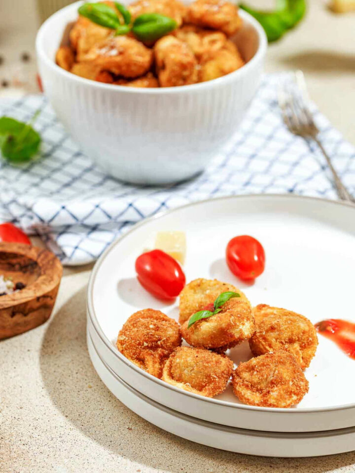 Fried tortellini served on a white plate with fresh cherry tomatoes and a side of marinara.