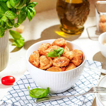 Close-up of parmesan-dusted fried tortellini in a white bowl with a fresh basil garnish