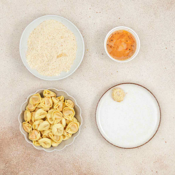 A top-down view of the breading station with raw tortellini, egg wash, and breadcrumbs.