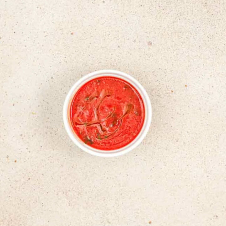 A small white bowl of red marinara sauce drizzled with olive oil.