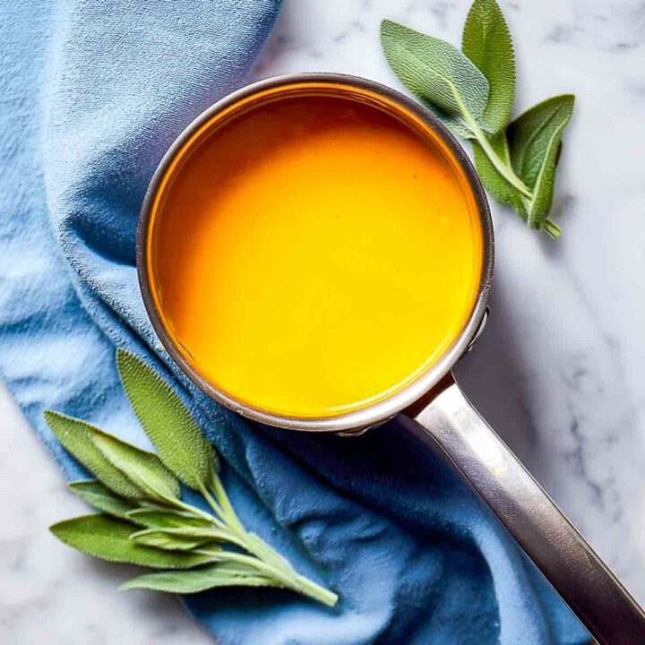 Bright pumpkin sauce in a stainless saucepan on marble with sage leaves.